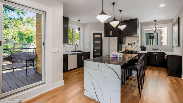 A modern kitchen with a marble island, pendant lighting, and a view to an outdoor deck. - Private Ultra Modern Mansion - Country Club Plaza (Kansas City)