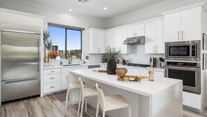 A modern kitchen with white cabinetry, stainless steel appliances, and a central island with seating. - Desert Standard • Modern 3-Level Desert Oasis • Steps to Old Town + Heated Pool (Scottsdale)