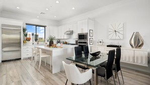 A modern kitchen with white cabinetry, a central island with seating, and a dining area with a glass table and chairs. - Desert Standard • Modern 3-Level Desert Oasis • Steps to Old Town + Heated Pool (Scottsdale)