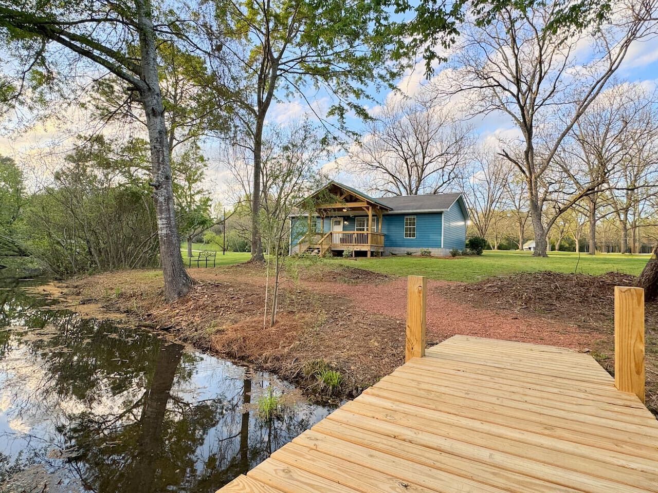 A house with a dock extending into a pond, surrounded by trees and a grassy area.