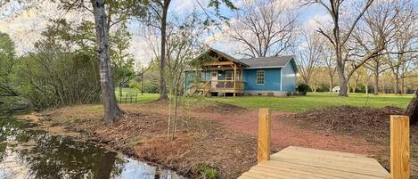 A house with a dock extending into a pond, surrounded by trees and a grassy area.