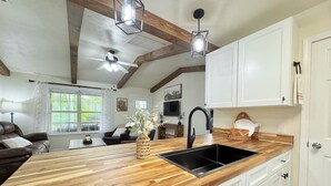 Une cuisine avec un plan de travail en bois, un évier noir et des armoires blanches. Un ventilateur de plafond et des luminaires suspendus sont installés au-dessus du plan de travail.