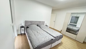 Une chambre à coucher avec un lit, une table de chevet avec une lampe, une armoire et une fenêtre avec des stores.