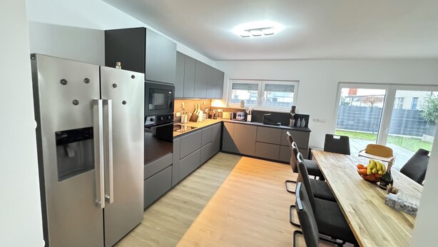 Une cuisine moderne équipée d’appareils électroménagers en acier inoxydable, une table à manger en bois et une vue sur le jardin.