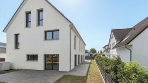 Une maison moderne à deux étages, dotée d’un toit plat, de grandes fenêtres et d’une allée pavée.