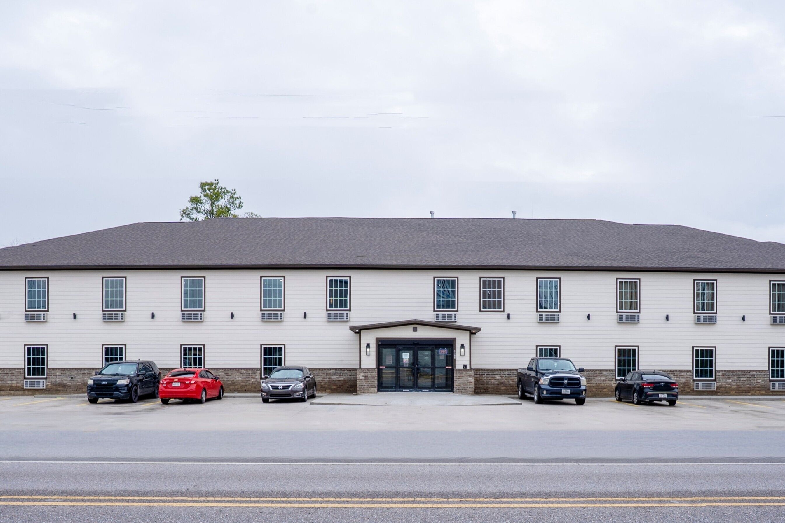 A building with a flat roof and a central entrance. There are six cars parked in front.