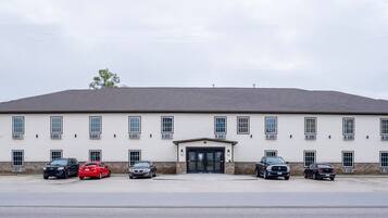 A building with a flat roof and a central entrance. There are six cars parked in front.