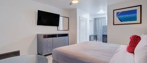 A hotel room with a bed, a desk, a ceiling fan, a TV mounted on the wall, and a framed picture on the wall.