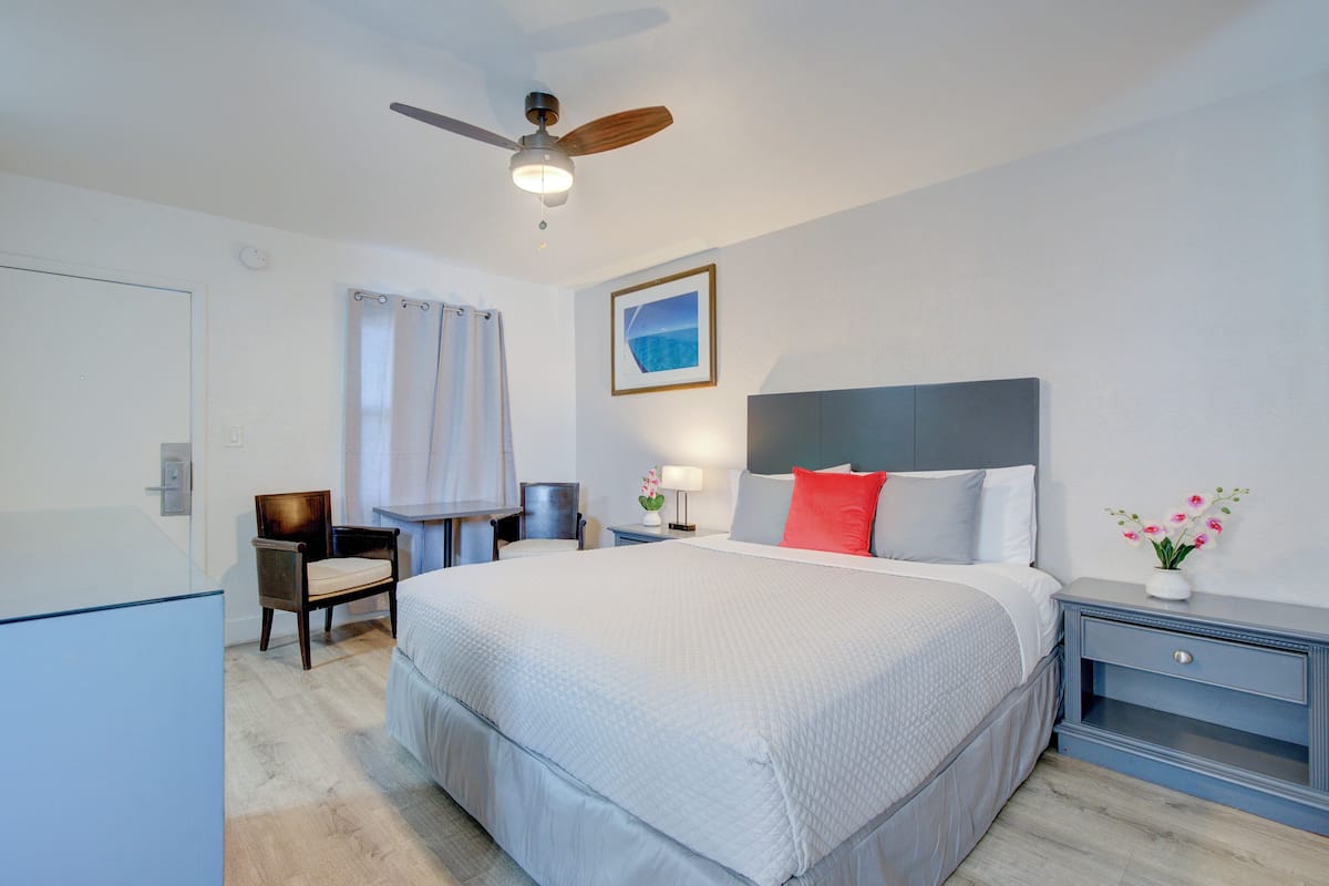 Une chambre bien rangée, avec un grand lit, une table de chevet, une chaise, un bureau et un ventilateur de plafond.