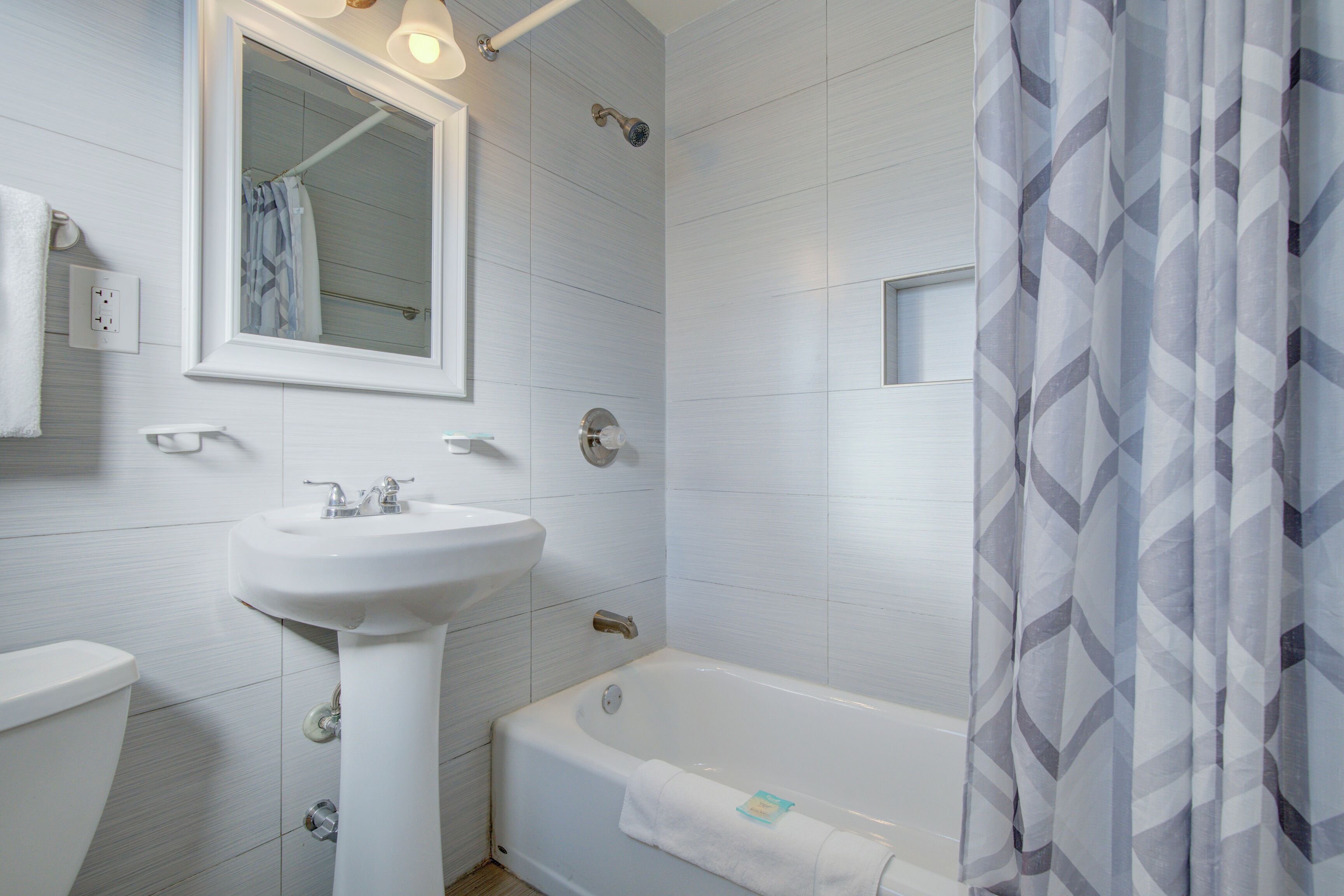 A bathroom with a white sink, mirror, and bathtub.