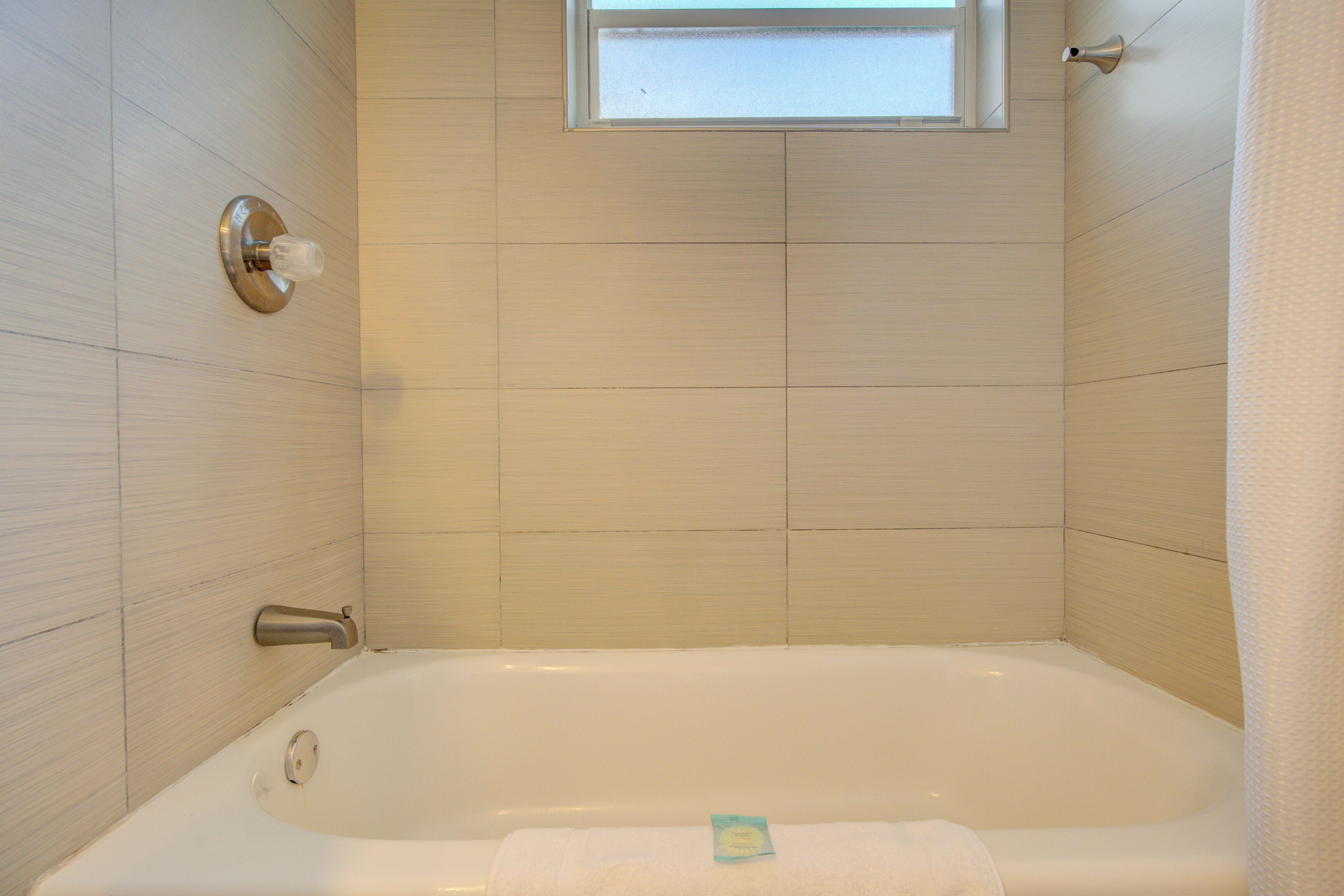 A modern bathroom with a bathtub, a window, and a towel rack.