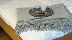 Ein Bett mit grauer Decke, ein Tablett mit einem Donut und zwei Gläsern sowie ein Kopfkissen mit Karomuster.