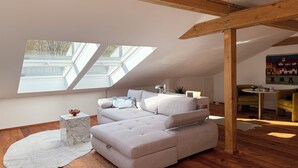 Ein modernes Schlafzimmer im Loft-Stil mit großem Dachfenster, Holzbalken, einer Couch, einem kleinen Tisch und einem Bild an der Wand.