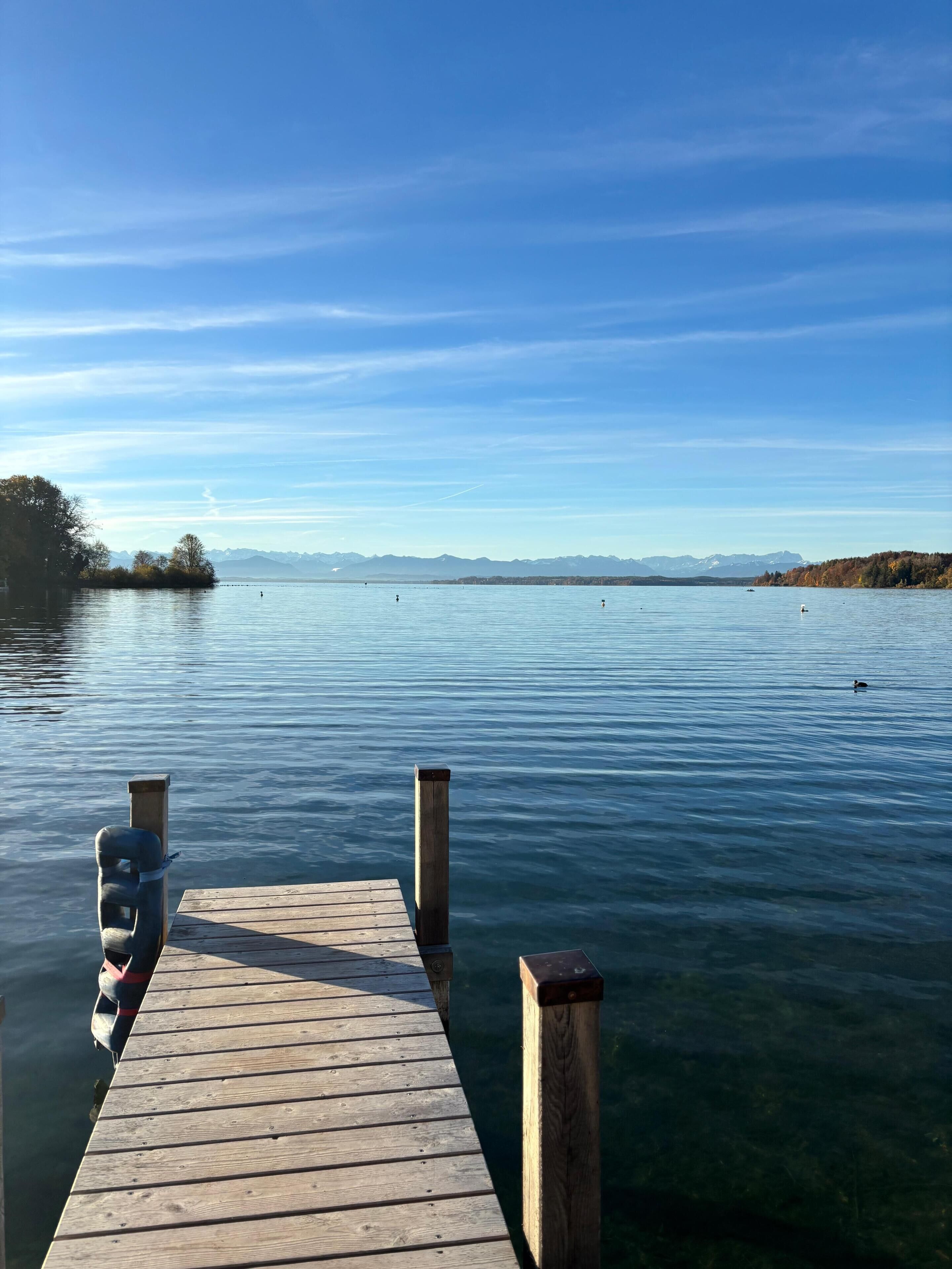 A wooden dock extending into calm water with a clear sky and distant mountains.
