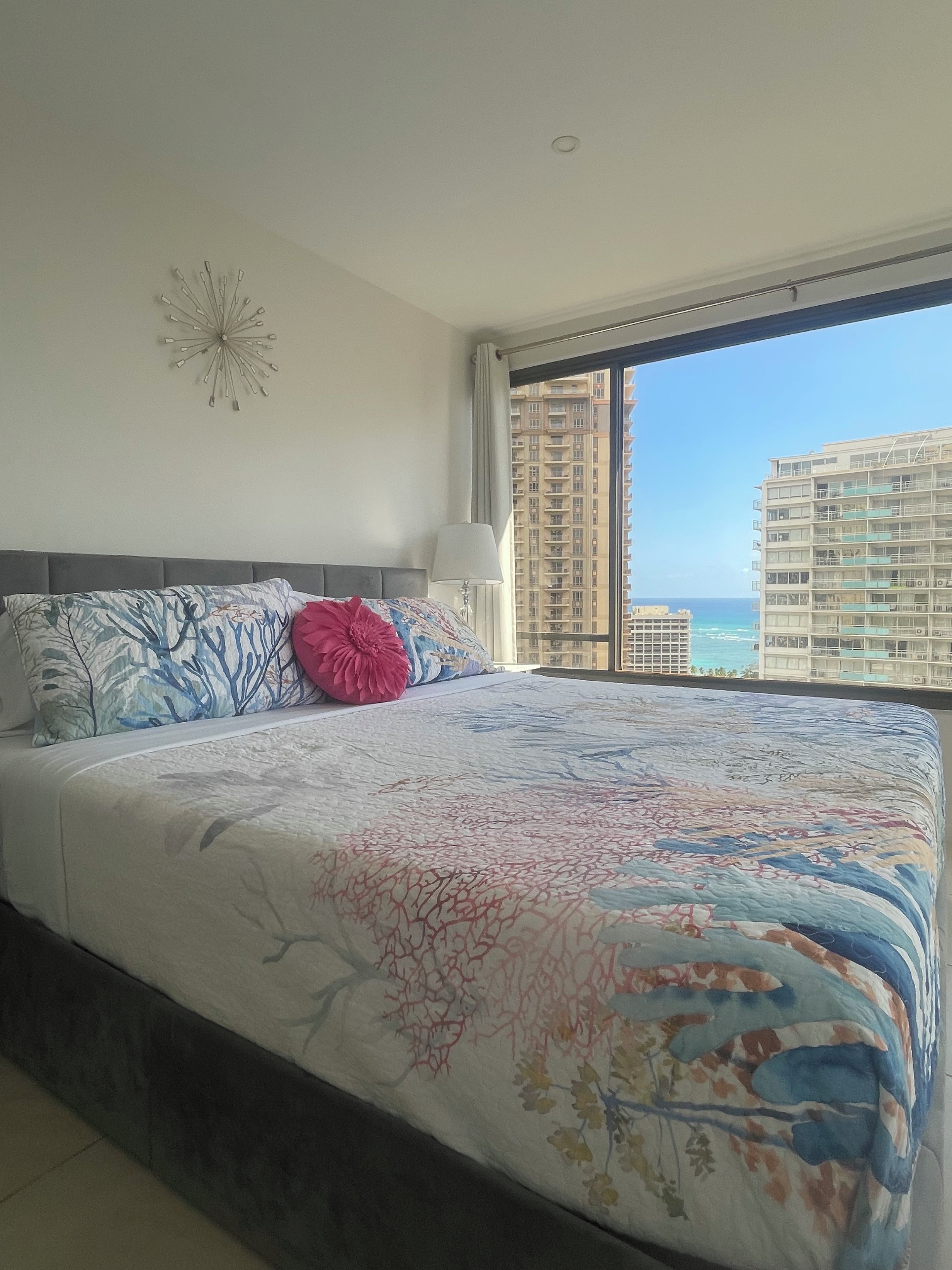 Un dormitorio con una cama grande, una ventana con vistas a edificios y al mar, y una decoración en la pared.