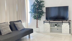 Un soggiorno moderno con un divano grigio, una TV a schermo piatto su un mobile bianco e una pianta in vaso.