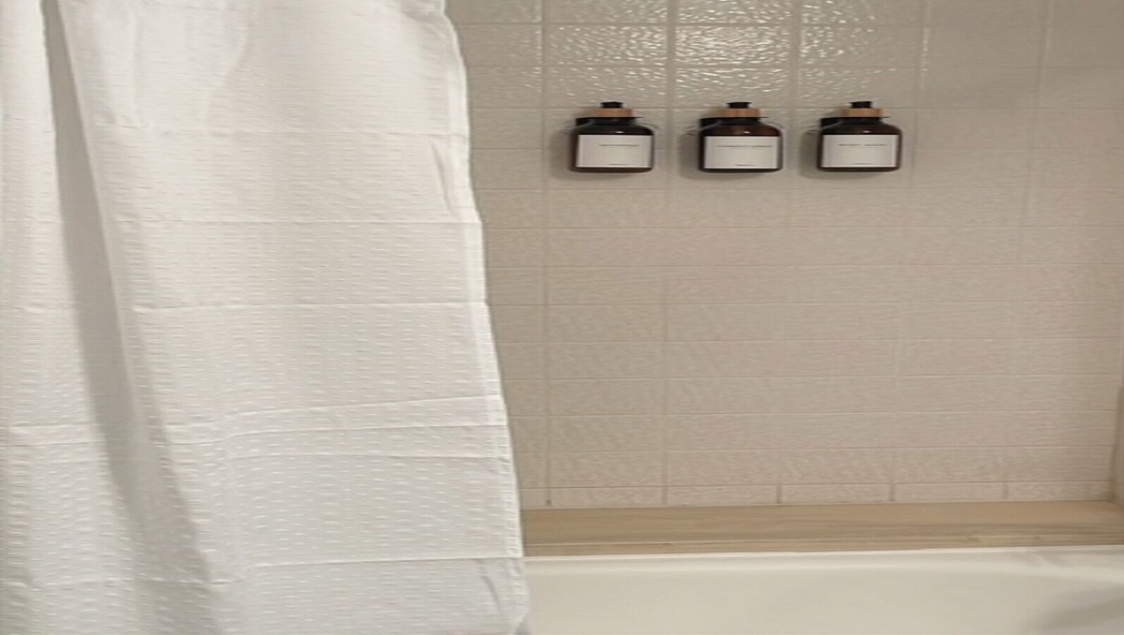 Une salle de bain avec un rideau de douche blanc, une baignoire et trois petites bouteilles accrochées au mur.