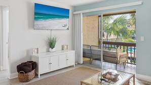 Un salón con televisor, mueble blanco, cesta de mimbre y una mesa de vidrio con adornos.