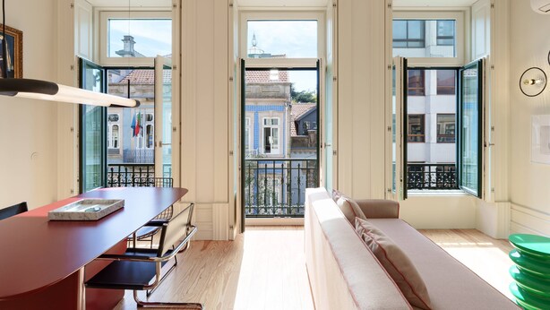 A room with a dining table, a sofa, and a view of the city through open doors. - VIVA - VIVA Quinta Modernista Flat (Porto)