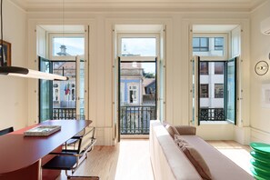 A room with a dining table, a sofa, and a view of the city through open doors. - VIVA - VIVA Quinta Modernista Flat (Porto)