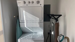 Una lavadora y secadora Whirlpool blancas y compactas en un lavadero pequeño con ventana que deja entrar luz natural.