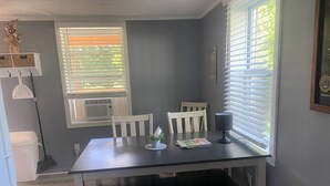 Un coin repas comprenant une table, des chaises et une fenêtre avec des stores.