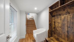 A hallway with a wooden staircase, a white chair, and a wooden cabinet with hooks. - Spacious 4BR Rittenhouse Square Retreat (Philadelphia)