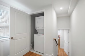 Une buanderie équipée d’un lave-linge et d’un sèche-linge, une porte donnant sur une autre pièce et une fenêtre avec des stores.