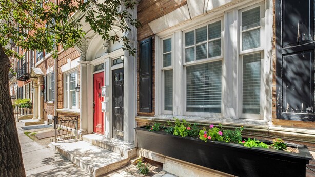 A row of townhouses with a red door, white window frames, and a planter box with flowers. - Spacious 4BR Rittenhouse Square Retreat (Philadelphia)