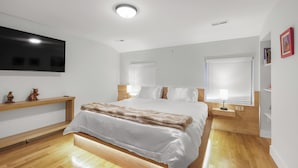 A modern bedroom with a large bed, wooden flooring, built-in shelving, and a flat-screen TV mounted on the wall. - Spacious 4BR Rittenhouse Square Retreat (Philadelphia)