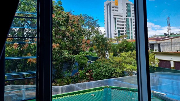 Vista a través de una ventana con tejado verde y un edificio alto al fondo.