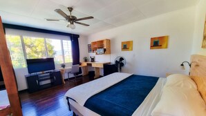 Un dormitorio con cama, escritorio, silla, ventilador de techo y ventana.