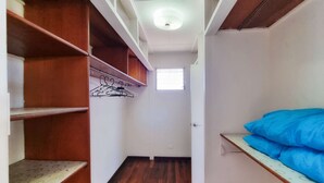 Un pasillo estrecho con estanterías de madera a la izquierda, una puerta blanca al final y un colchón azul a la derecha.