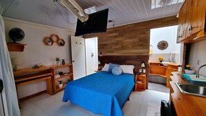 Une chambre à coucher comprenant un lit, des tables de chevet, un bureau, une télévision et une salle de bain avec un lavabo et un miroir.