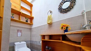 Une petite salle de bain comprenant des toilettes, des étagères en bois, un miroir et un lavabo.