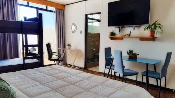 A hotel room with a large bed, a desk with chairs, a TV, and a balcony. - 714 Studios (San José)