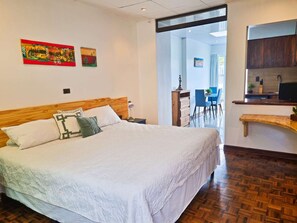 Une chambre d’hôtel avec un grand lit, une tête de lit en bois, un bureau avec une chaise et un coin cuisine.