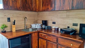 A compact kitchen with wooden cabinets, a stainless steel sink, a coffee maker, and a built-in dishwasher. - 714 Studios (San José)