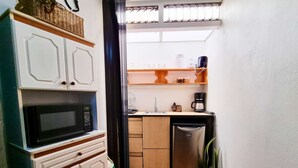 Une cuisine compacte avec des meubles blancs, un four à micro-ondes, un lave-vaisselle et un petit plan de travail sur lequel se trouve une machine à café.