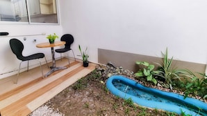 Een klein terras met een houten tafel en twee zwarte stoelen, een klein blauw waterpartij en diverse potplanten.
