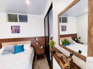 A hotel room with two beds, a wooden headboard, a mirror, a nightstand, a small table with a plant, and a wall-mounted artwork. - 714 Studios (San José)