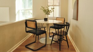 A dining area with a round table, four chairs, a vase with flowers, and a painting on the wall.