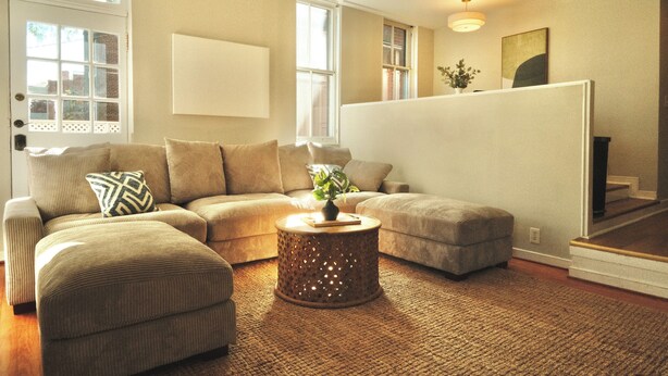 A living room with a sectional sofa, ottoman, and a round coffee table with a plant.