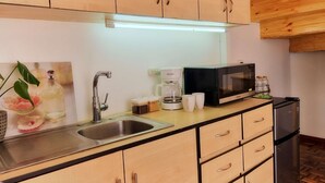 Een keuken met houten kasten, een roestvrijstalen spoelbak, een magnetron en een koelkast.