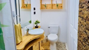 Een kleine badkamer met een houten wastafelmeubel, een witte wasbak, een toilet en een spiegel met planken erboven.