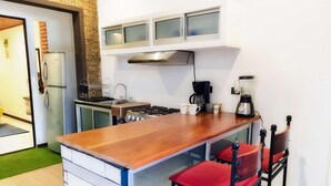 Een kleine keuken met een houten aanrecht, een gasfornuis, een koffiezetapparaat en een blender. Er staan twee rode stoelen en een klein spoelbakje.