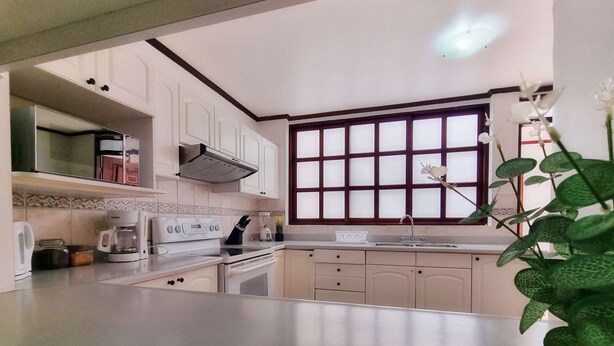 Una cocina con armarios blancos, estufa, lavamanos y ventana con vidrios esmerilados.