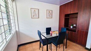 Un comedor con mesa y sillas de vidrio, dos obras de arte enmarcadas en la pared y un mueble de madera con estantes.