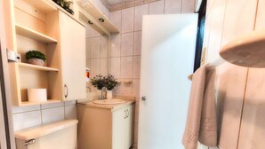 Une salle de bain équipée de toilettes, d’un lavabo et d’étagères où sont rangés les articles de toilette.
