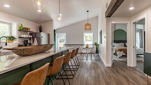 Een moderne keuken met een groot keukenblok, barstoelen, hanglampen en uitzicht op de eethoek.